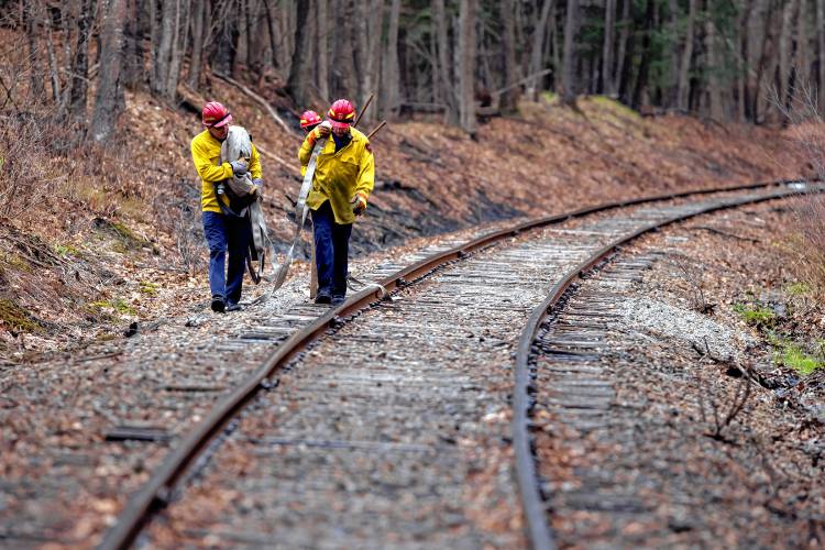 Concord firefighters carry hoses along the railroad tracks off of Sewalls Falls Road on Wednesday, April 24, 2024 to battle a four acre brush fire along the Merrimack River.